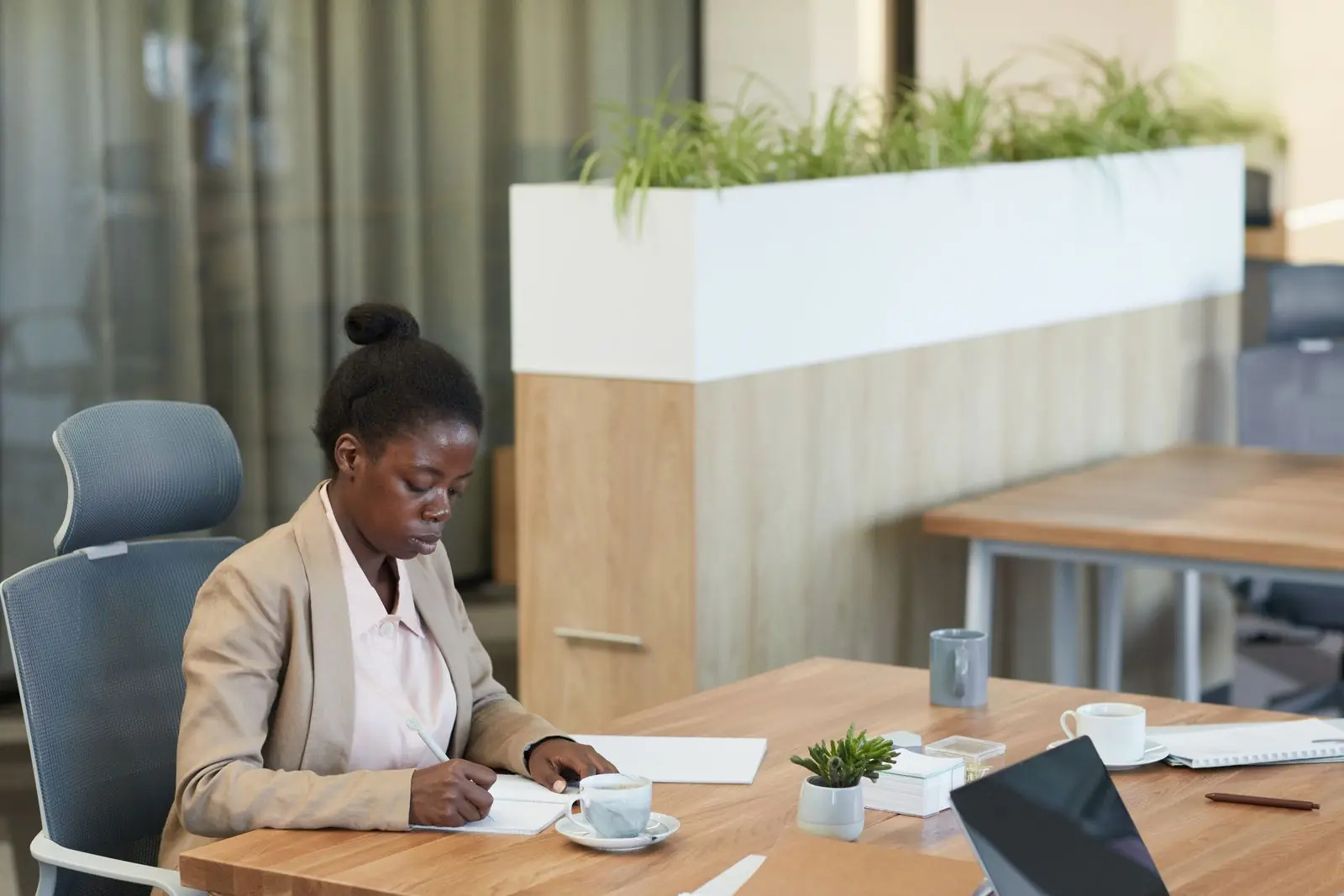 Une consultante prend des notes à son bureau, café et tablette à portée de main