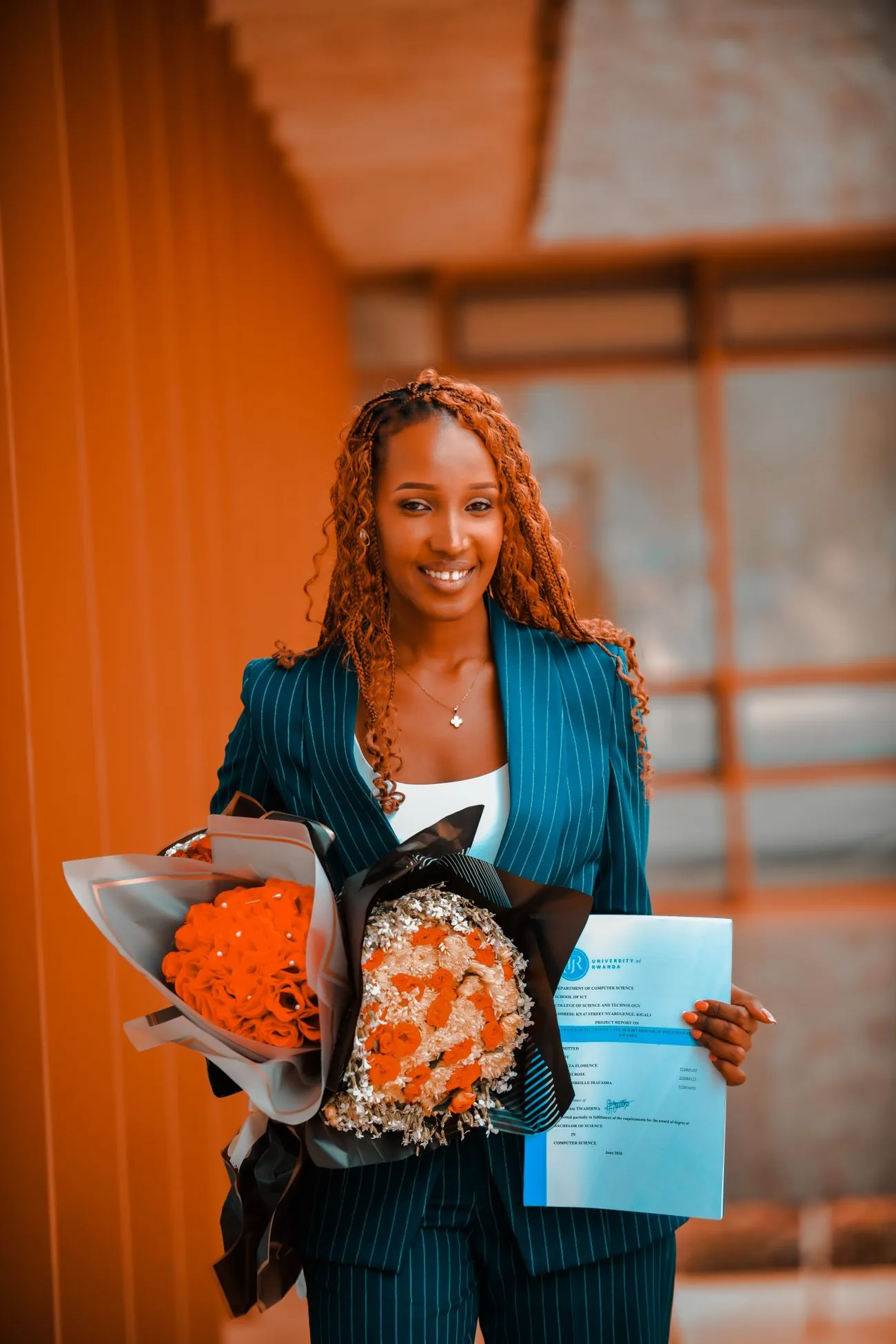 Une jeune femme souriante, en tailleur, qui tient un bouquet de fleurs et un diplôme